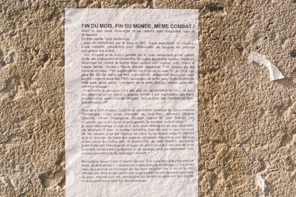 a manifesto (in French, in small type) plastered to a light-colored stone wall