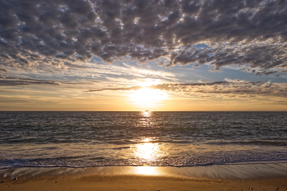 grey cloudy sky over the beach with sun setting at horizon