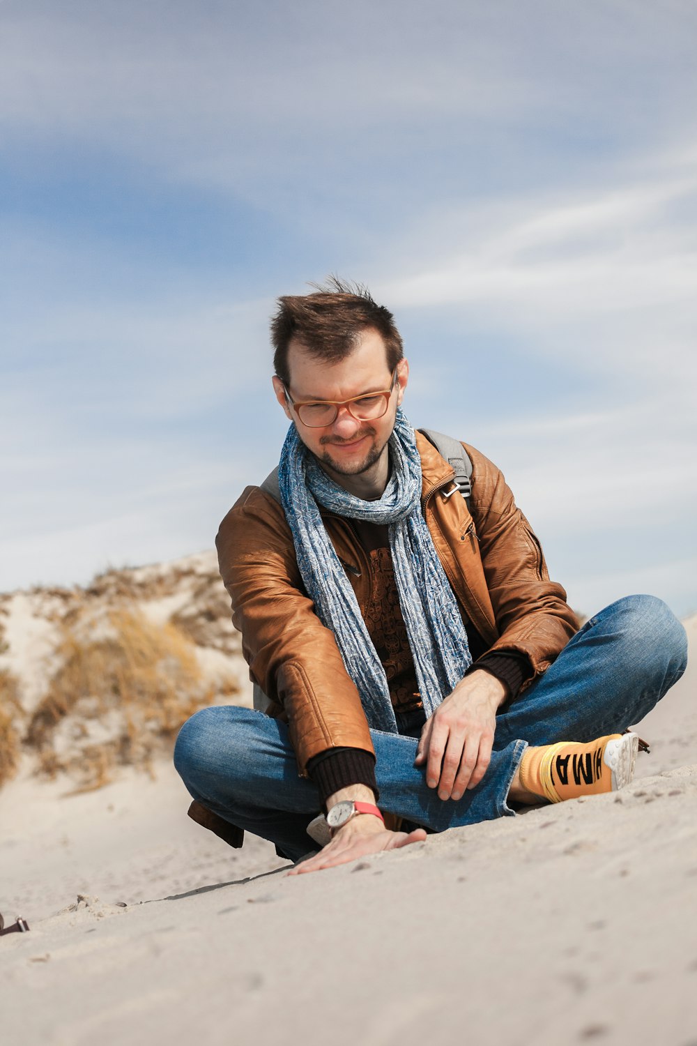 smiling man sitting on ground and touching sand under blue and white skies