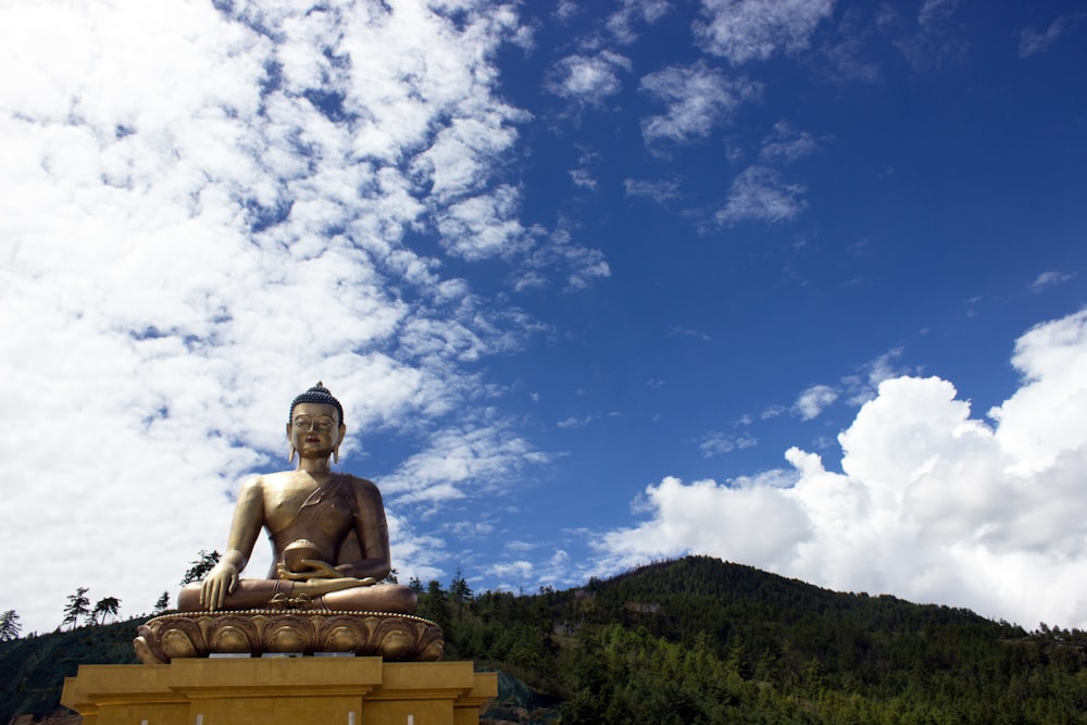 Buddha sitting statue viewing mountain under blue and white skies