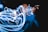 A person is partly visible, surrounded by a chaotic swirl of bright, blue and white light trails against a dark background. The light gives a dynamic and energetic feel, almost as if the person is manipulating electricity.