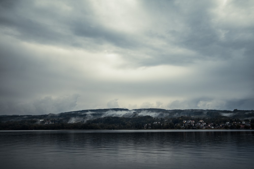 body of water near mountain under clouds