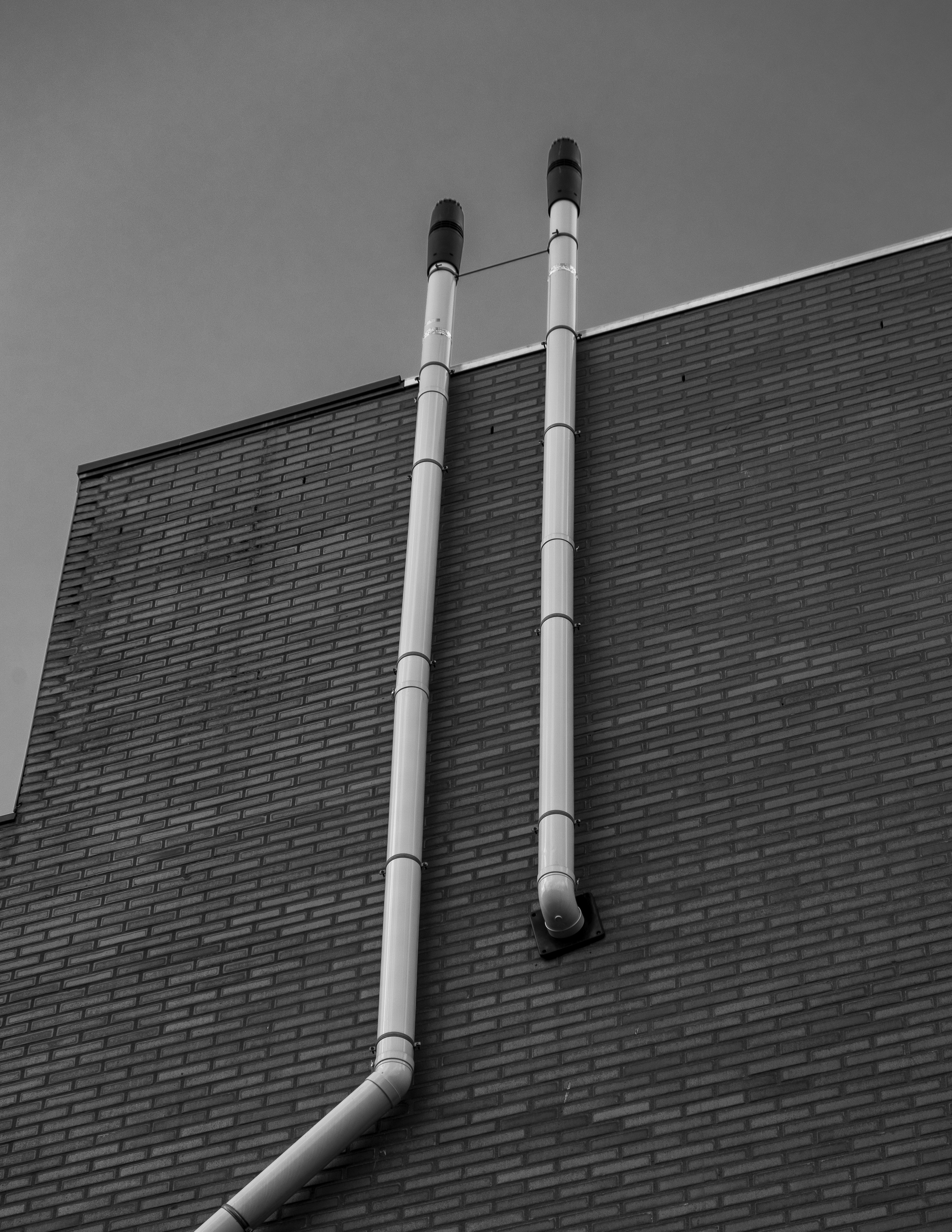 Pair of white PVC pipes sticking out of brick wall photo Free Grey