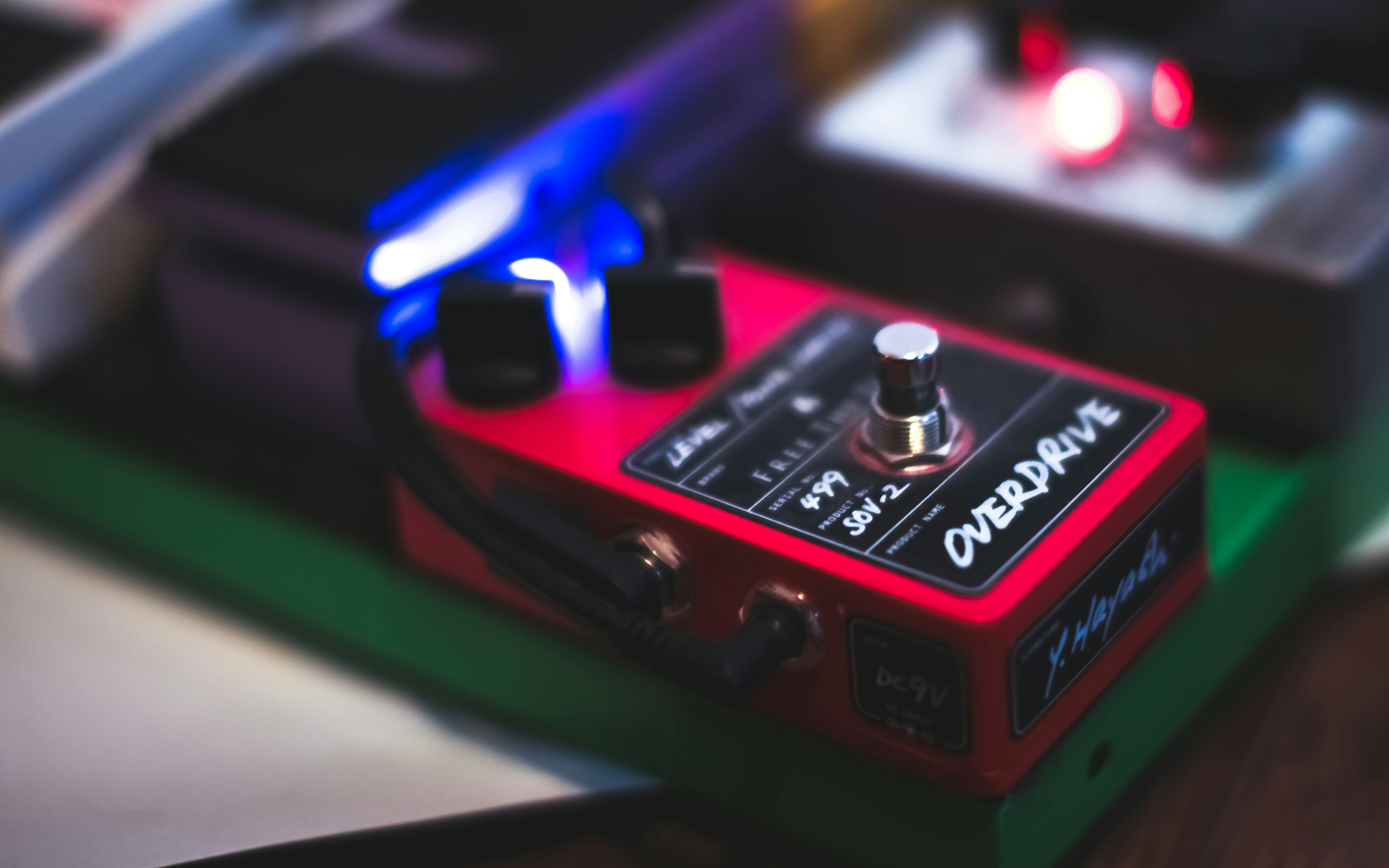Pedał efektów gitarowych typu overdrive, leżący na podłodze obok wzmacniacza, symbolizujący rozwiązanie problemu głośnego brzmienia.