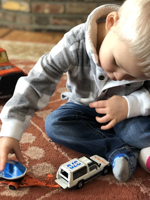 boy sitting on carpet playing car toys