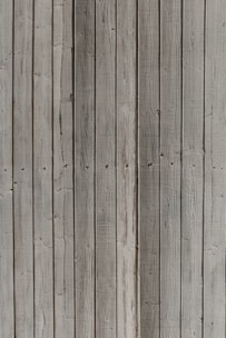 Vertical wooden planks with a weathered appearance, featuring natural textures and patterns formed by grain and knots.