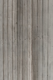Vertical wooden planks with a weathered appearance, featuring natural textures and patterns formed by grain and knots.