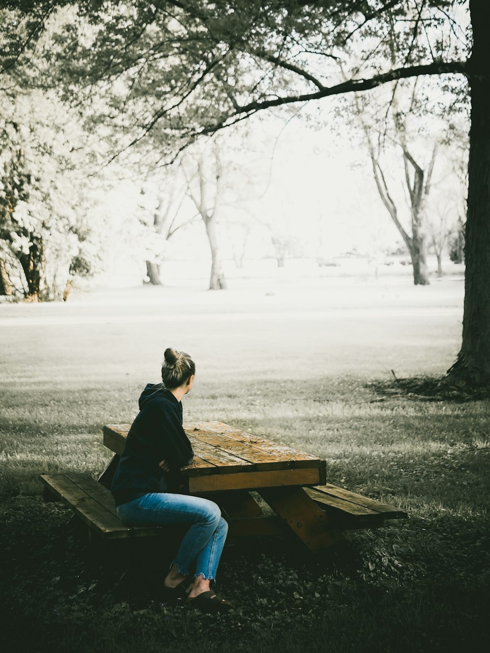 woman in black hoodie and blue denim jeans sitting on picnic bench
