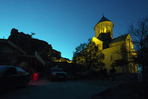 The church exterior at twilight, warmly lit, with families arriving for evening service