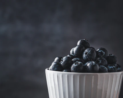 Close-up of a cozy ceramic bowl with a glossy, deep green glaze, holding fresh fruit.