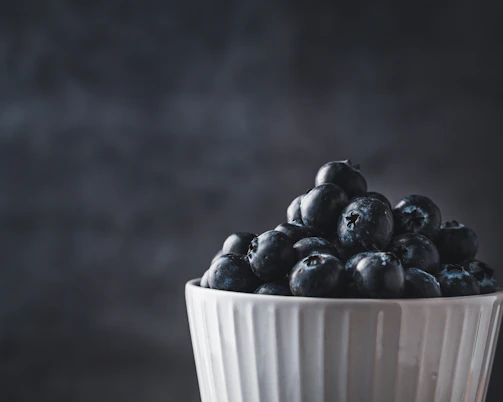 Close-up of a deep teal ceramic bowl with subtle speckles, filled with fresh berries, highlighting the smooth glaze and organic shape.