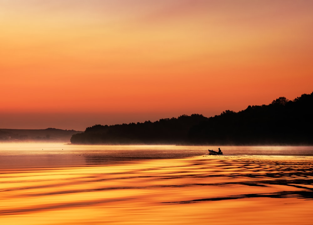 Hombre en barco en el mar durante la puesta del sol con el cielo naranja