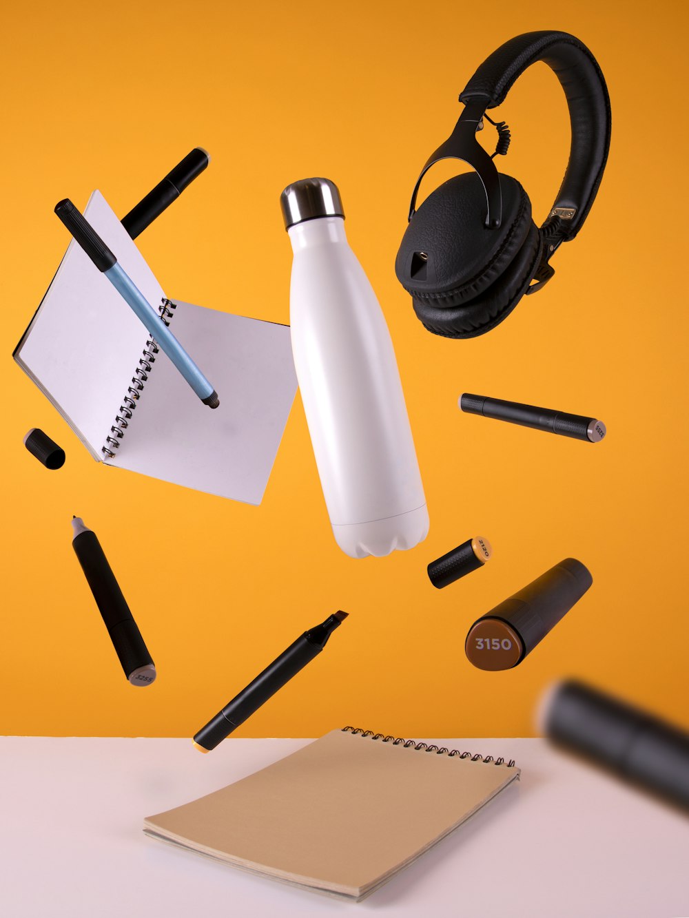 black cordless headphones beside sport bottle and notebook