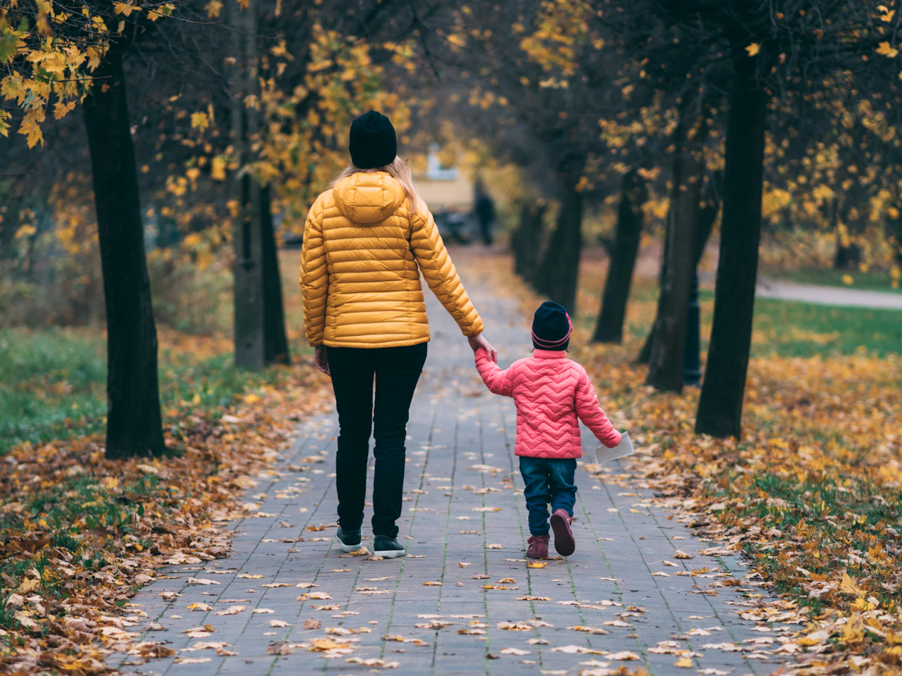 A mother and daughter walking together along an autumn path