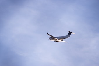 A small propeller airplane is flying in a clear blue sky. The aircraft appears well-lit by sunlight, and it is captured from beneath, showing its wings and undercarriage.