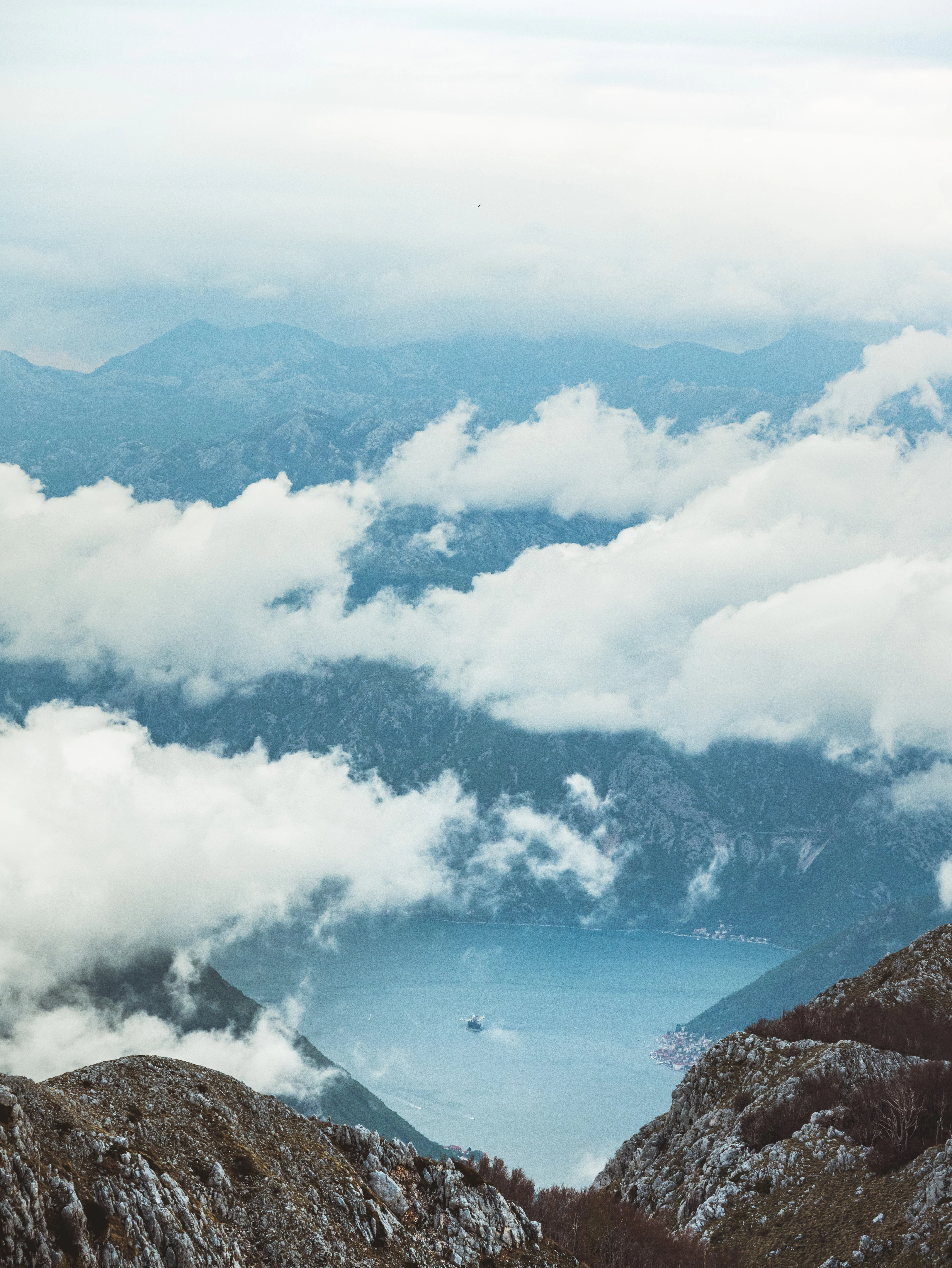 Layers of cloud part to reveal a narrow blue bay far below jagged peaks.