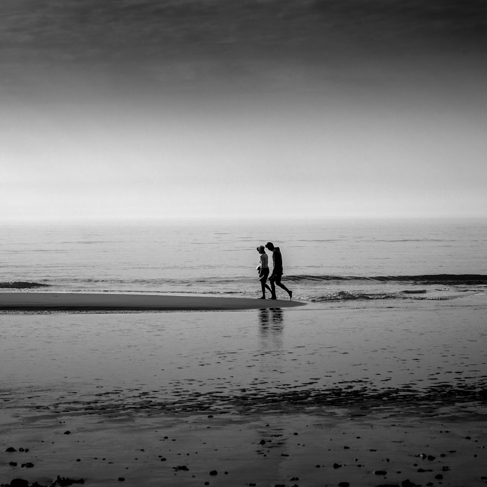 grayscale photography of two person walking on seashore