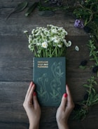 woman holds Familiar Wild and Flowers book on common daisies on brown panel