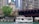 A tour boat named 'Chicago's Little Lady' travels along a river, surrounded by the architectural features of a cityscape. There is a large bridge overhead with people observing the scene, and a lush green tree on the riverbank next to historic architectural structures.