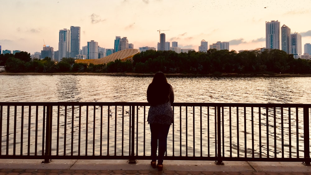 woman standing in front of body of water and city buildings