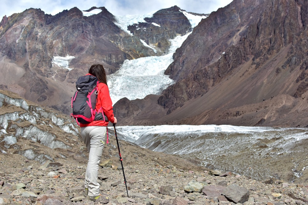 woman in red jacket, white pants, and black backpack