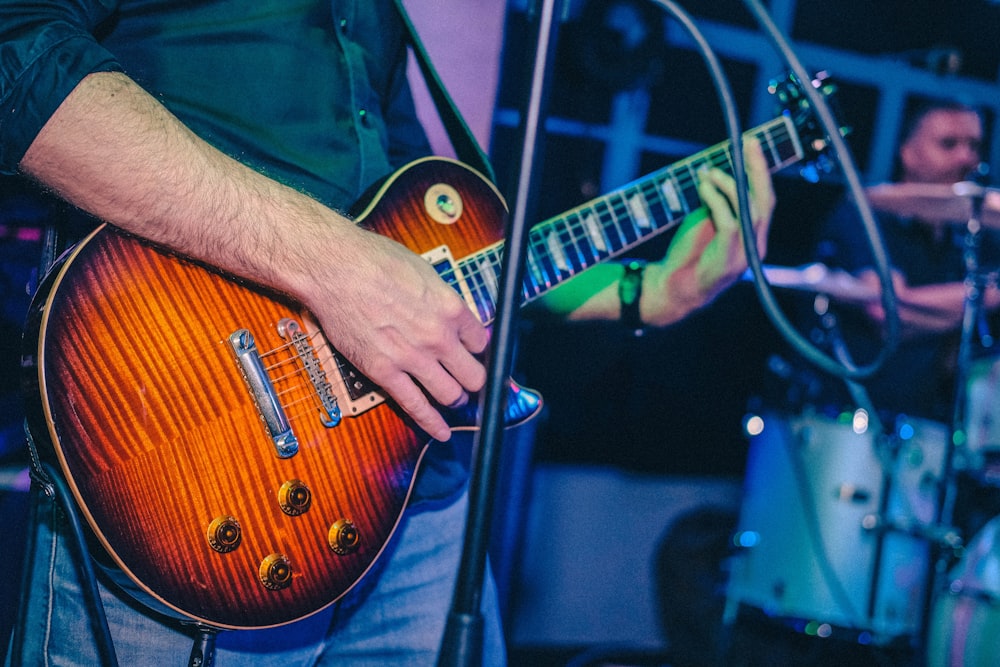 man standing and playing electric guitar near another man playing drums