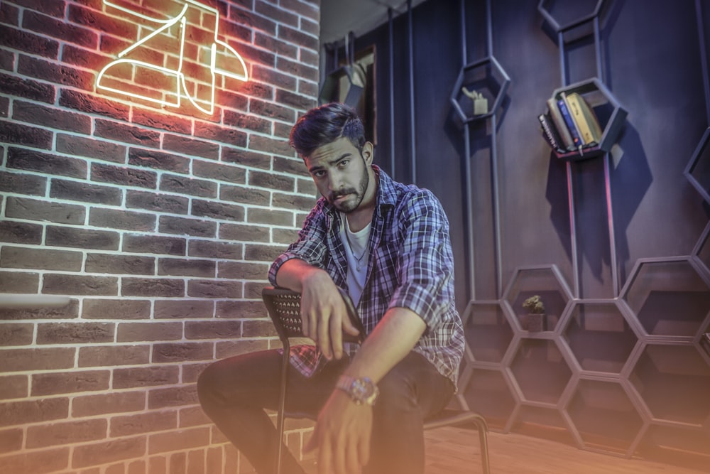 man sitting on chair beside brick wall