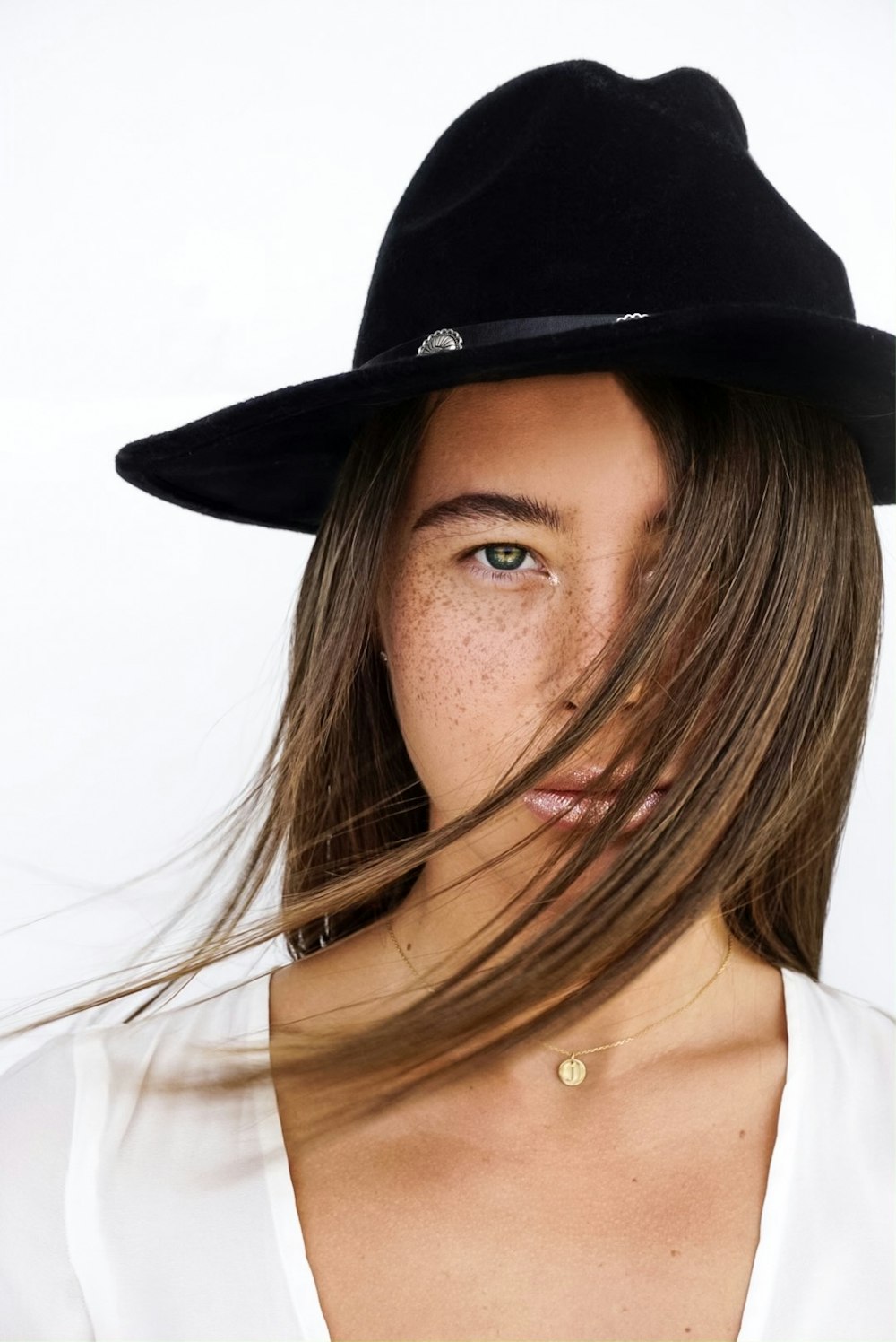 woman wearing white scoop-neck shirt and black hat covering her face with her hair