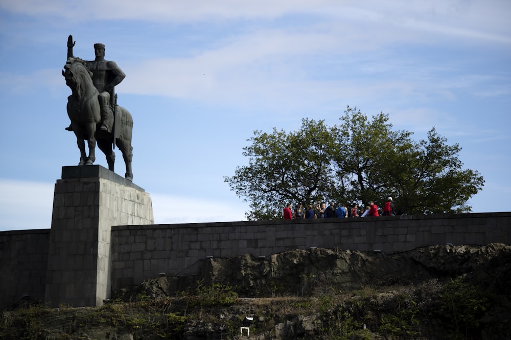 people walking near green tree beside man riding horse statue under blue and white skies