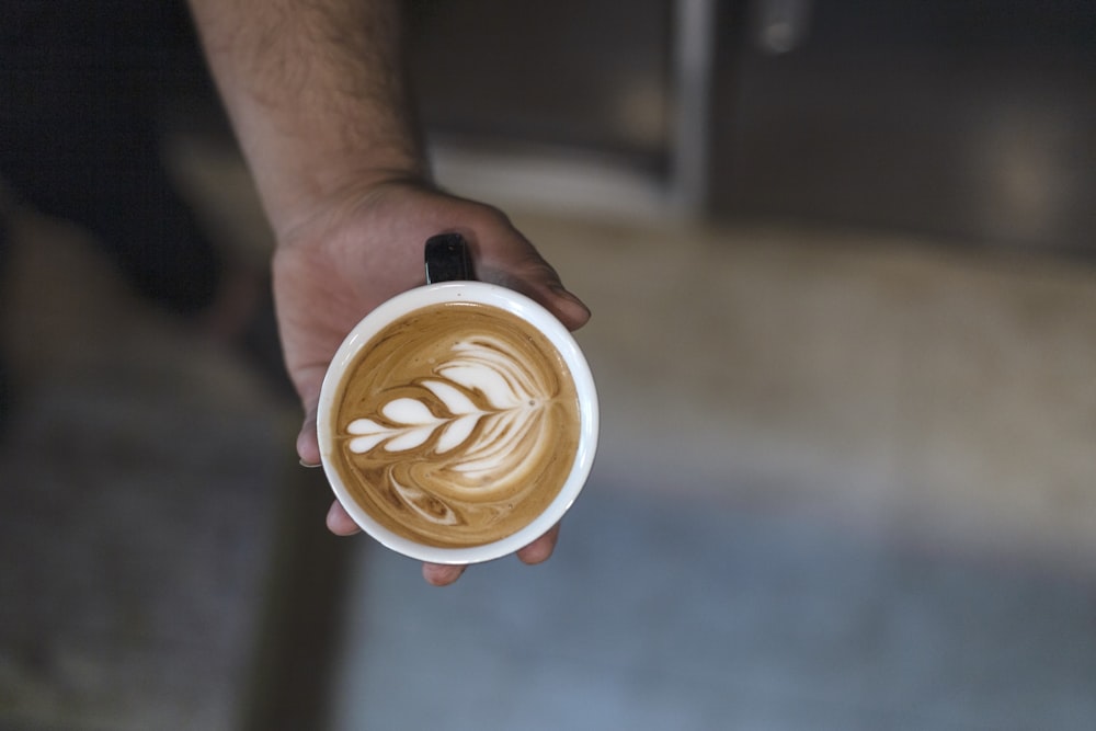 Persona sosteniendo un café con leche de hoja