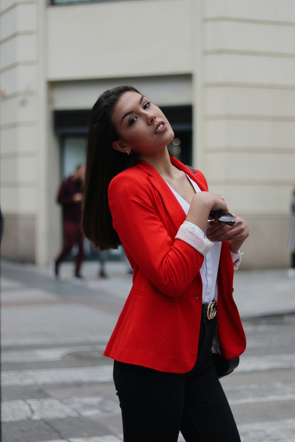 woman in white shirt and black fitted pants with red blazer crossing street