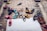 A variety of sandals and flip-flops are scattered on a brick pavement, including different colors like black, blue, pink, yellow, and brown. Some of the sandals have playful designs, while others are more plain. The arrangement appears random, suggesting a cluttered or casual scene.