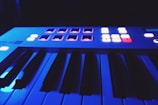 Close-up of synthesizer keys glowing under dim purple light.