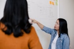 two women standing in front of white dry erase board