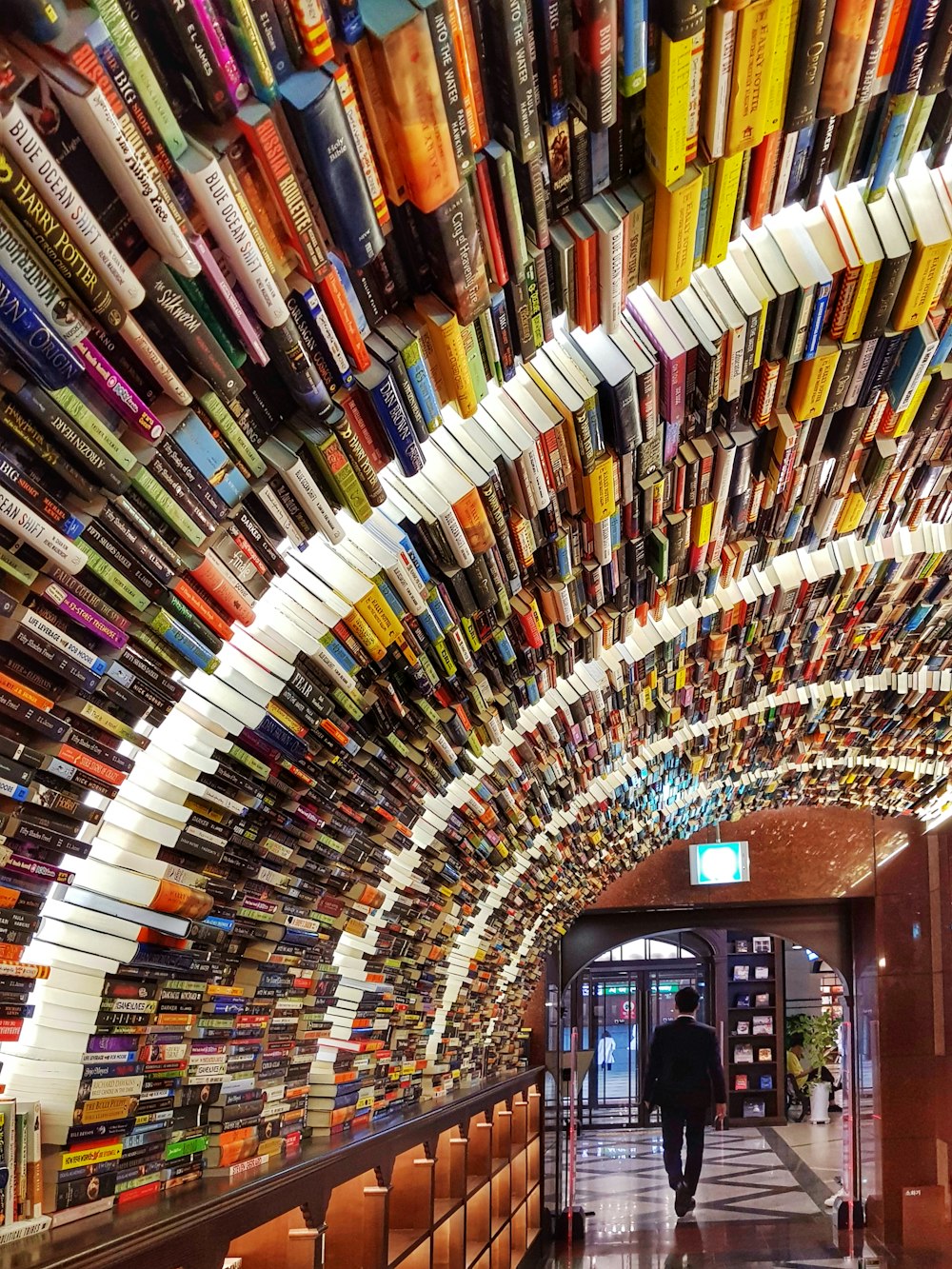 man in black suit walking by the piled of books