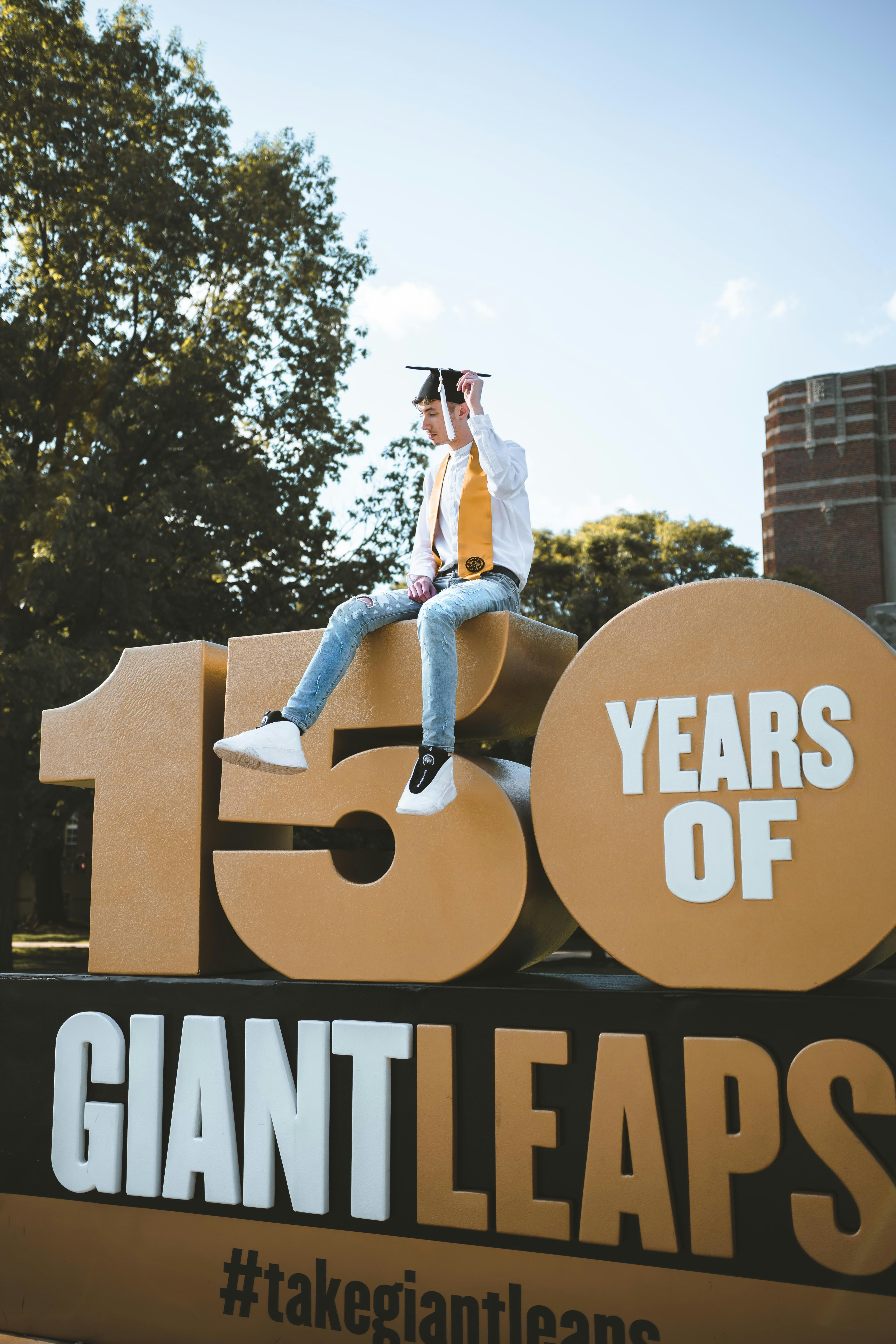 Man with black mortar board sitting on 150 years giant leaps building