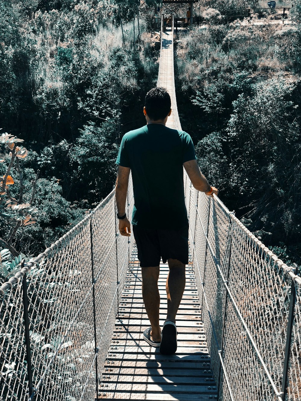 man in green t-shirt and black pants crossing hanging footbridge