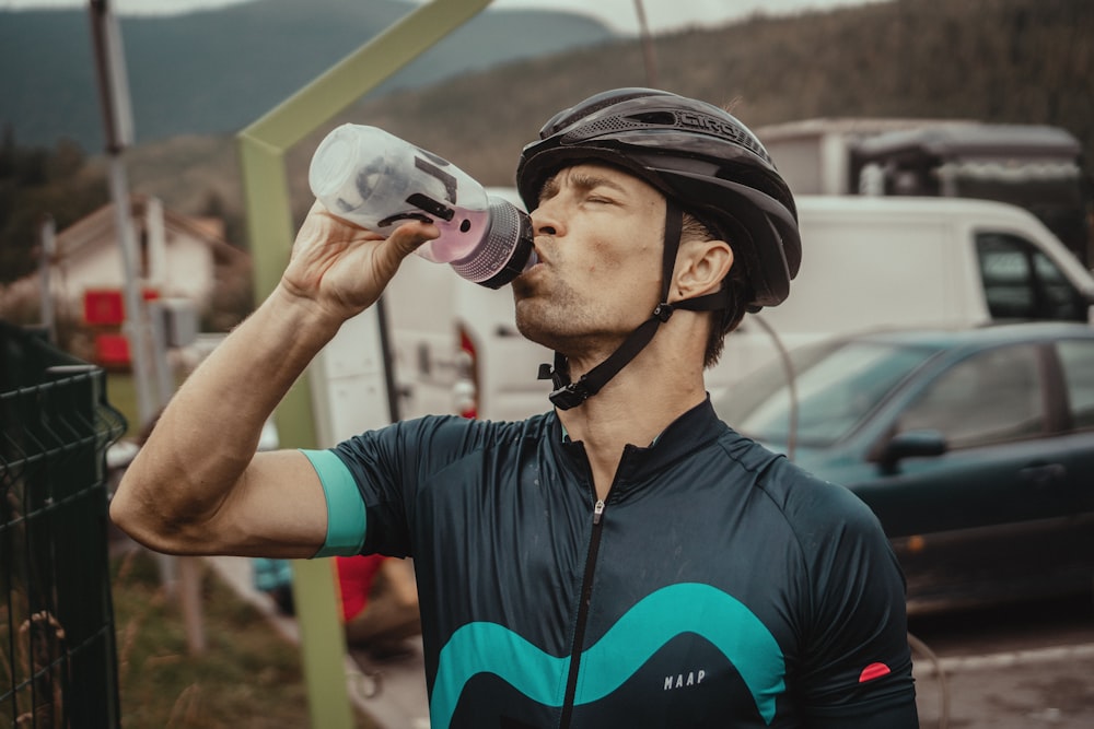 man drinking from a sports bottle wearing biking gear in front of parked cars