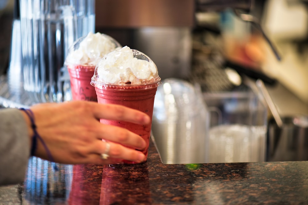 two ice cream in disposable cups with clear caps on marble surface