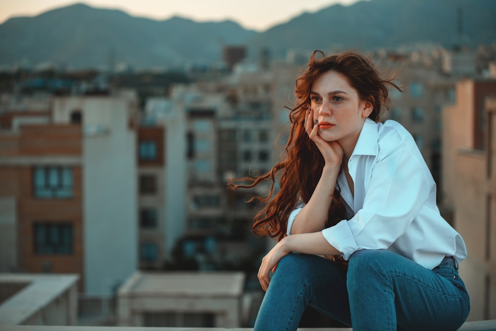 woman in white dress shirt and blue denim jeans sitting at rooftop