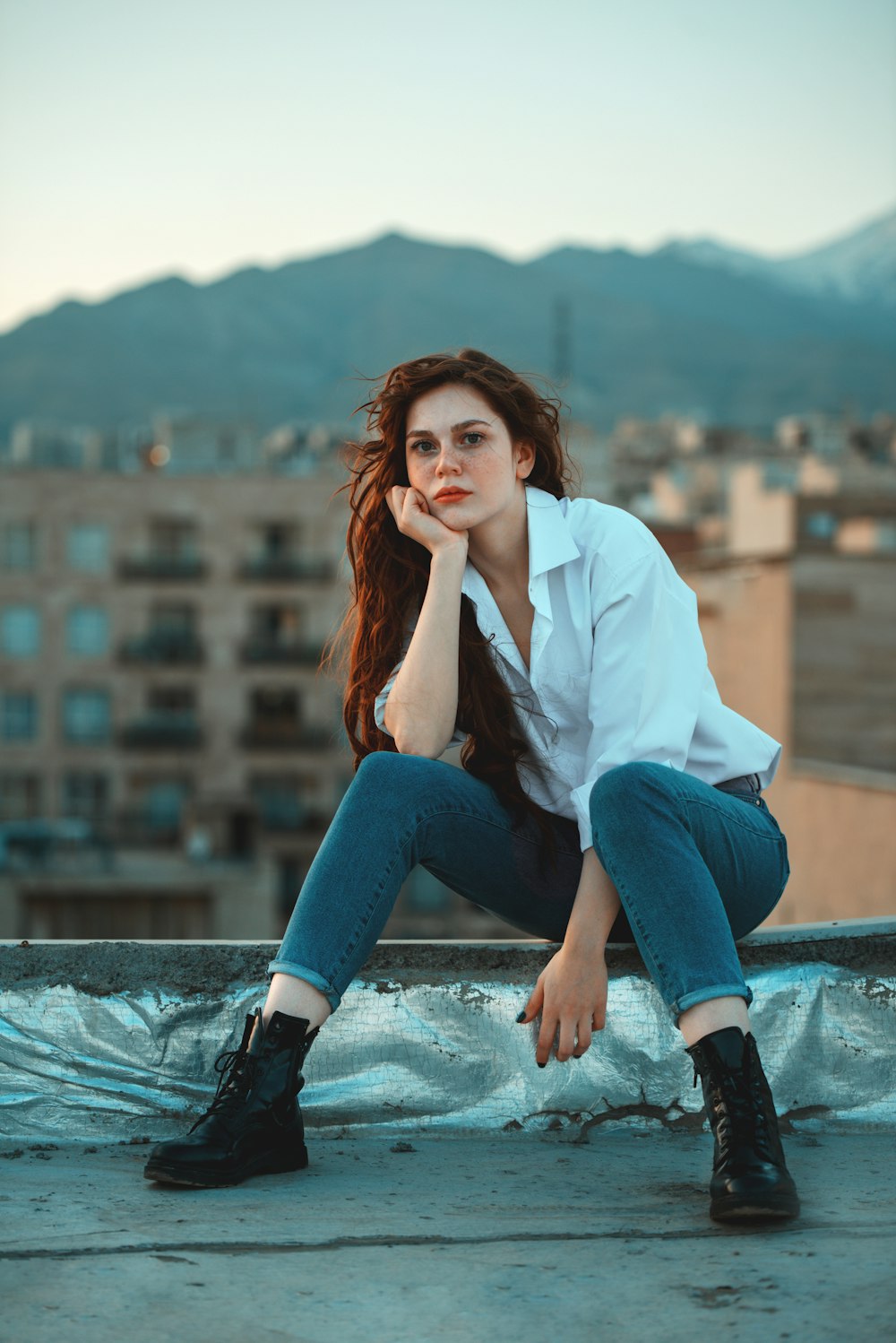 woman in white dress shirt and blue denim jeans sitting at rooftop