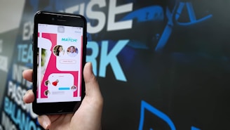 A hand holding a smartphone displaying a mobile app interface with a 'Match' notification. The screen shows profile pictures and chat options in a colorful design. The background is blurred with large text in blue and white.
