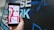 A hand holding a smartphone displaying a mobile app interface with a 'Match' notification. The screen shows profile pictures and chat options in a colorful design. The background is blurred with large text in blue and white.