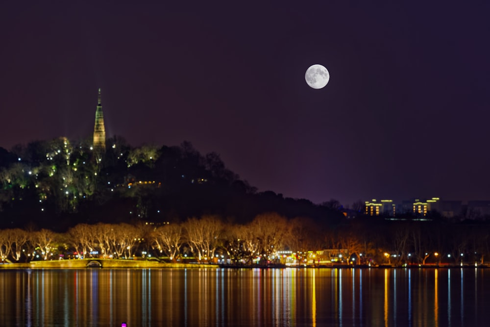 white round moon in dark night sky over lighted city skyline by the bay