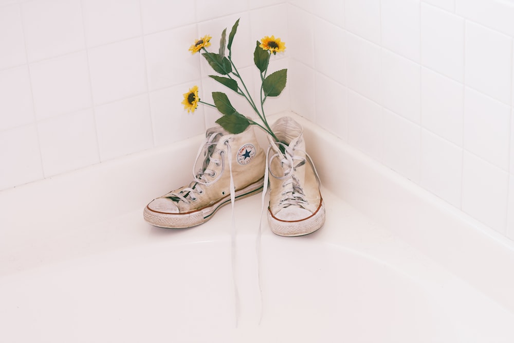 blooming yellow sunflower on white Converse high-top sneakers near white wall tiles