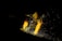 A person in a dark environment is engaged in welding, wearing protective clothing and a helmet. Bright sparks fly around, illuminating parts of the person and the workspace.