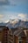 A breathtaking view of snow-capped mountains in the background under a partly cloudy sky. In the foreground, modern wooden chalets with dark roofs and multiple balconies add a cozy alpine touch.