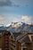 A breathtaking view of snow-capped mountains in the background under a partly cloudy sky. In the foreground, modern wooden chalets with dark roofs and multiple balconies add a cozy alpine touch.