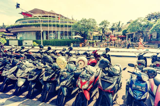 A row of colorful scooters parked on a sunlit beach with palm trees swaying in the background.
