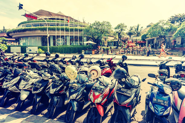 A row of colorful scooters parked on a sunlit beach with palm trees swaying in the background.